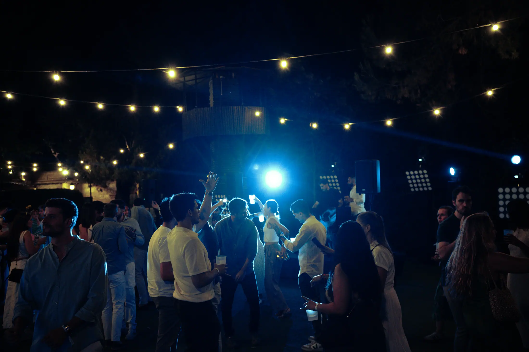 Multitud bajo iluminación azul y decoración con bombillas, noche de evento