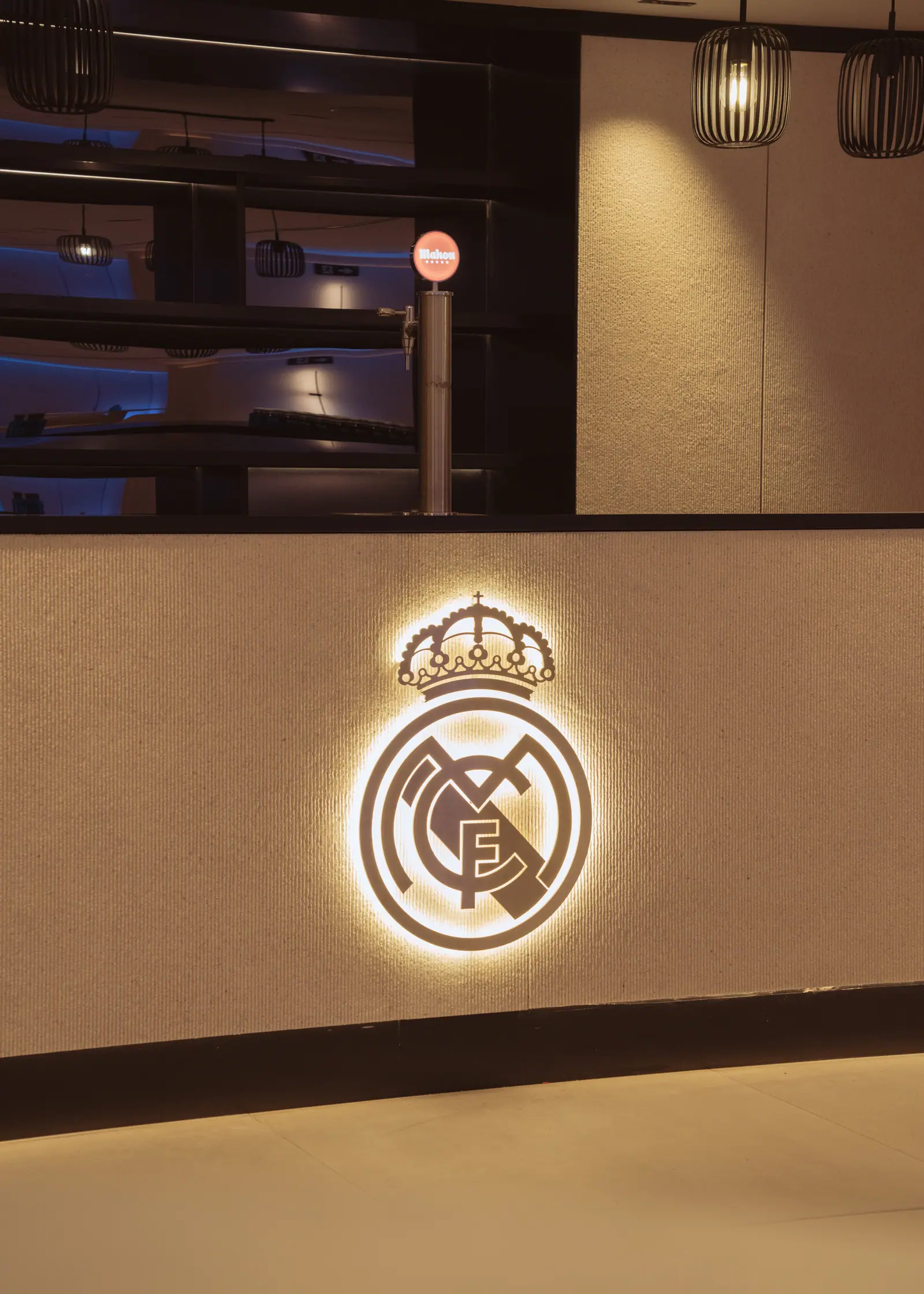 Escudo del Real Madrid en neon dorado iluminado sobre pared de piedra texturizada