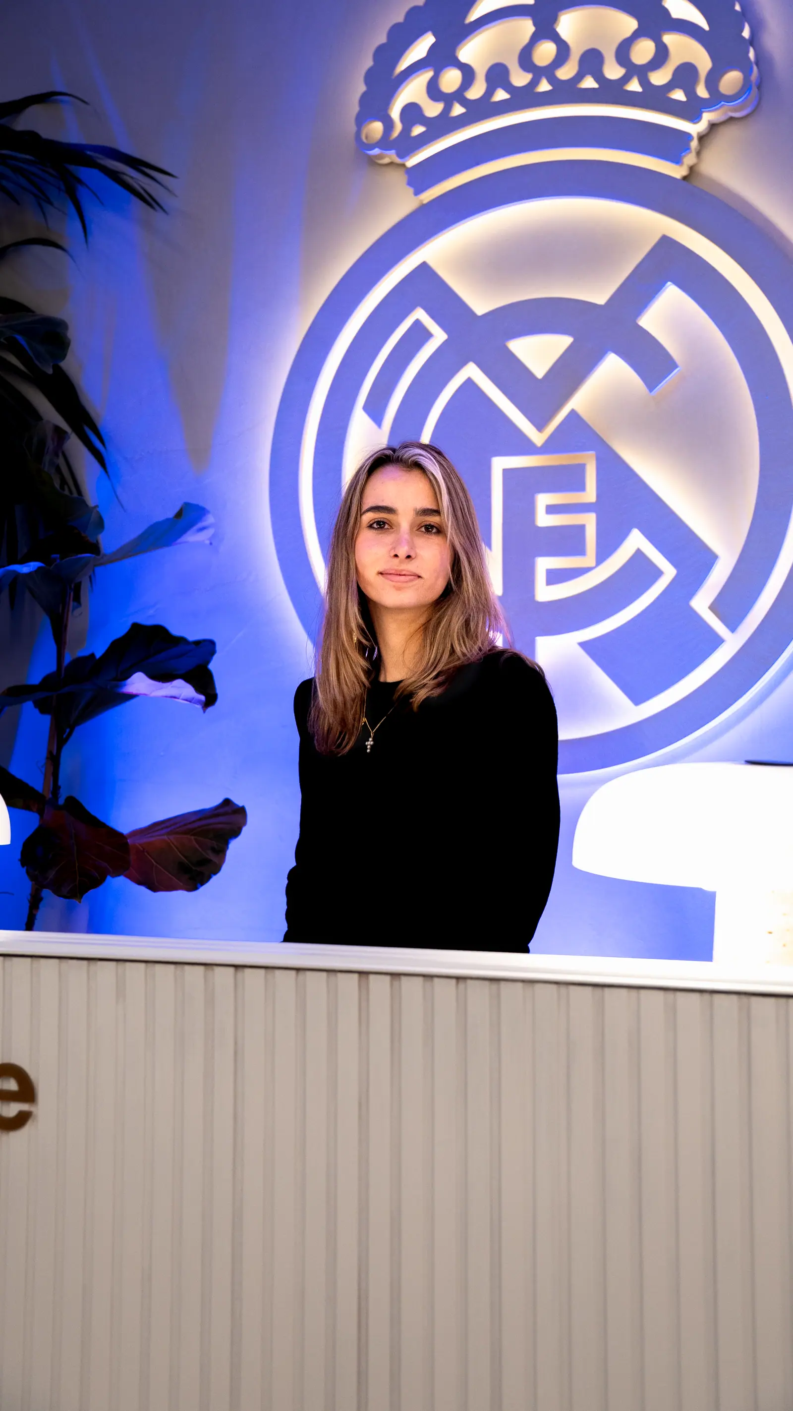 Presentadora profesional en cabina DJ con escudo de Real Madrid iluminado en neon azul al fondo.